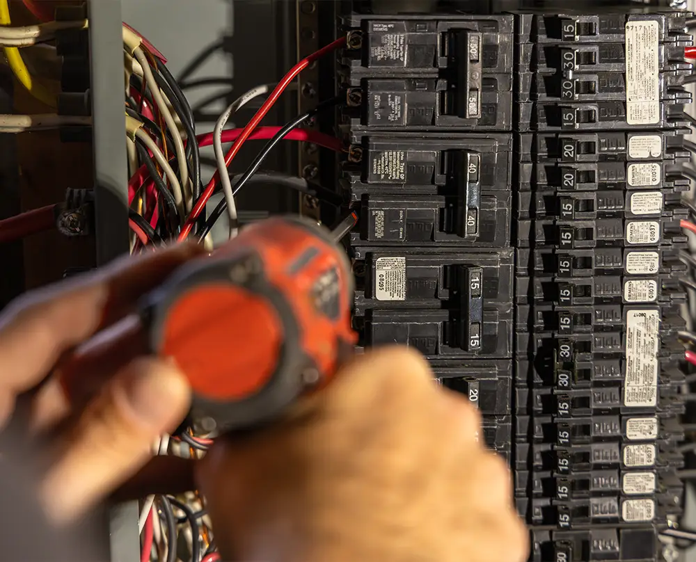 Hands using a power tool inside an electrical panel with exposed wiring and circuit breakers in Belleville, IL.