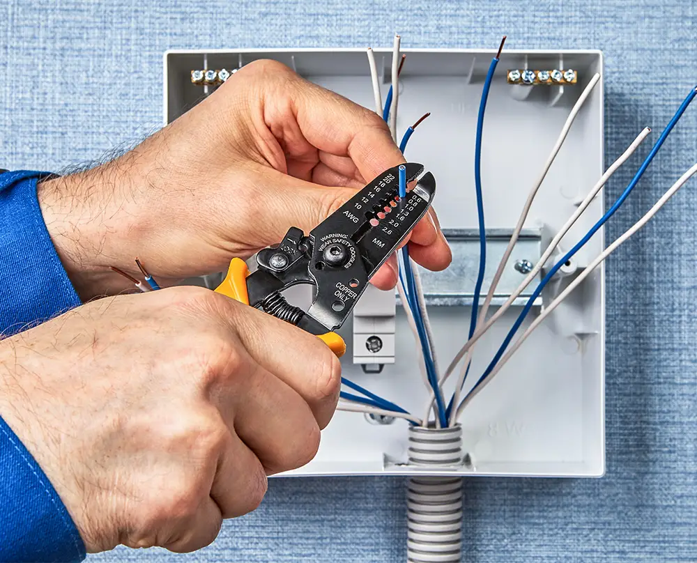 Hands using wire strippers to prepare electrical wiring inside an open electrical box in Belleville, IL.