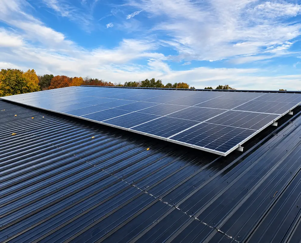 Solar panel array mounted on a dark metal roof beneath a partly cloudy sky in Belleville, IL and the Metro East.